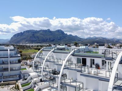 Edificio de apartamentos contemporáneo con fachadas blancas curvas, terrazas con barandillas de cristal y césped artificial, y vistas a la sierra.