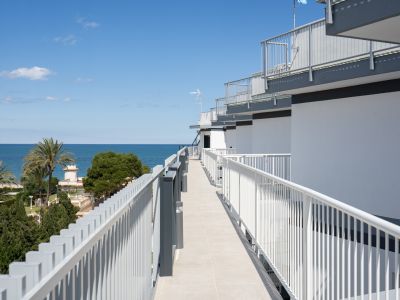 Pasillo exterior con suelo de baldosas claras y barandillas modernas, ofreciendo vistas directas al mar Mediterráneo y palmeras.