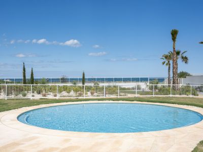 Piscina circular con borde pavimentado, rodeada de césped y un jardín mediterráneo con palmeras, ofreciendo vistas al mar.