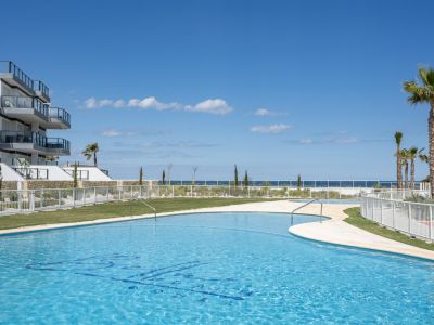 Piscina comunitaria de diseño curvo con vistas al mar, rodeada de zonas verdes y la moderna fachada del edificio de apartamentos.