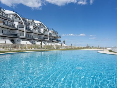 Piscina exterior azul vibrante en un complejo moderno con arquitectura curva y balcones de cristal, frente al mar.