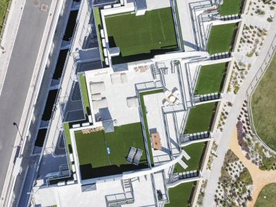 Vista aérea de terrazas en azotea con césped artificial, mobiliario exterior y áreas de descanso, junto a senderos y piscina.