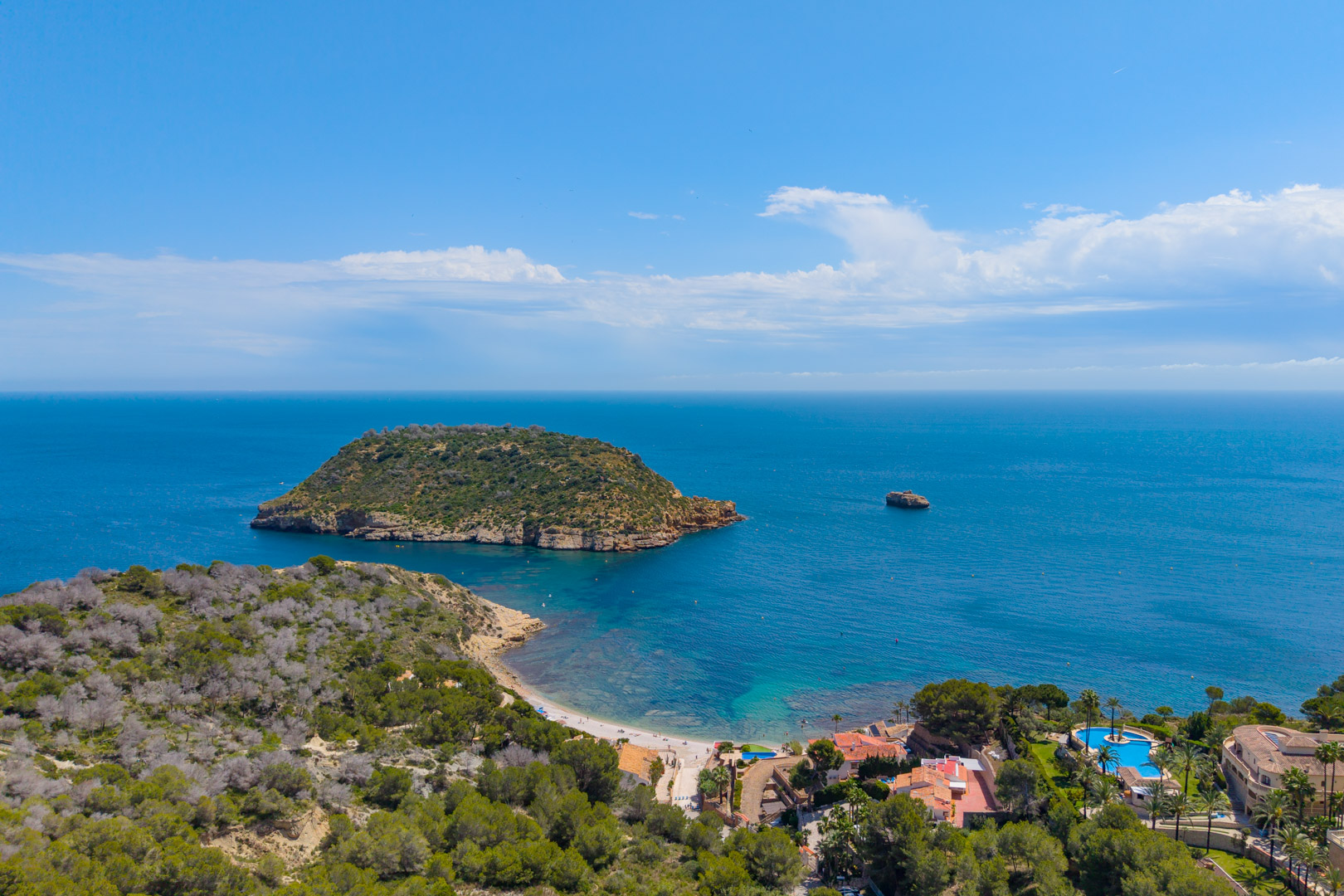 Vista aérea de la costa de Jávea con la Isla del Descubridor, playa, y zona residencial con piscina.