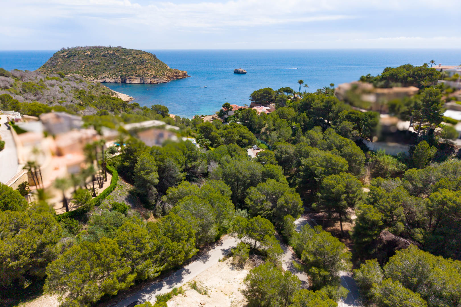 Vista aérea de la parcela arbolada con acceso por carretera, con vistas al mar y al cabo en Jávea.