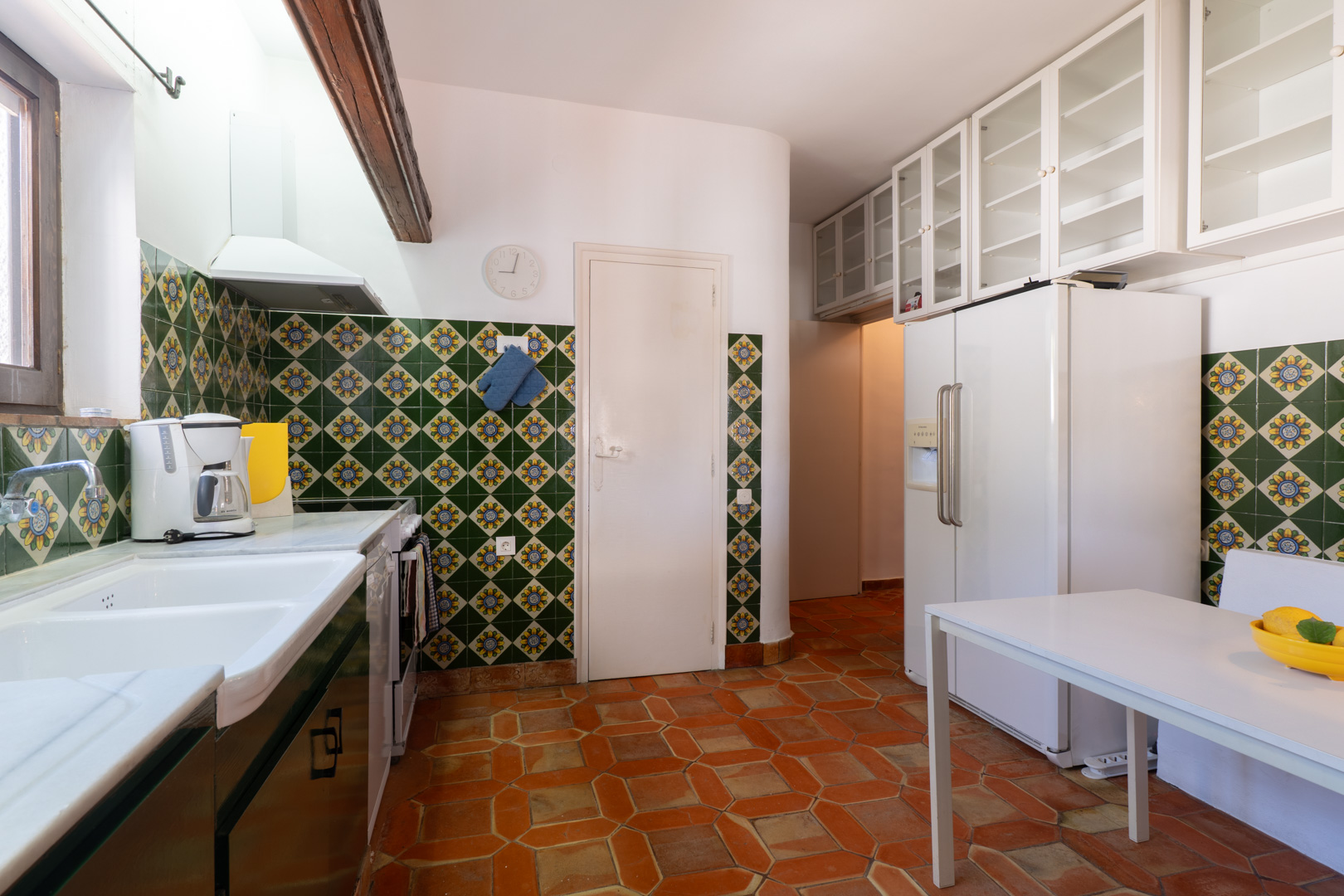 Cocina con azulejos decorativos, suelo de terracota y armarios altos blancos.