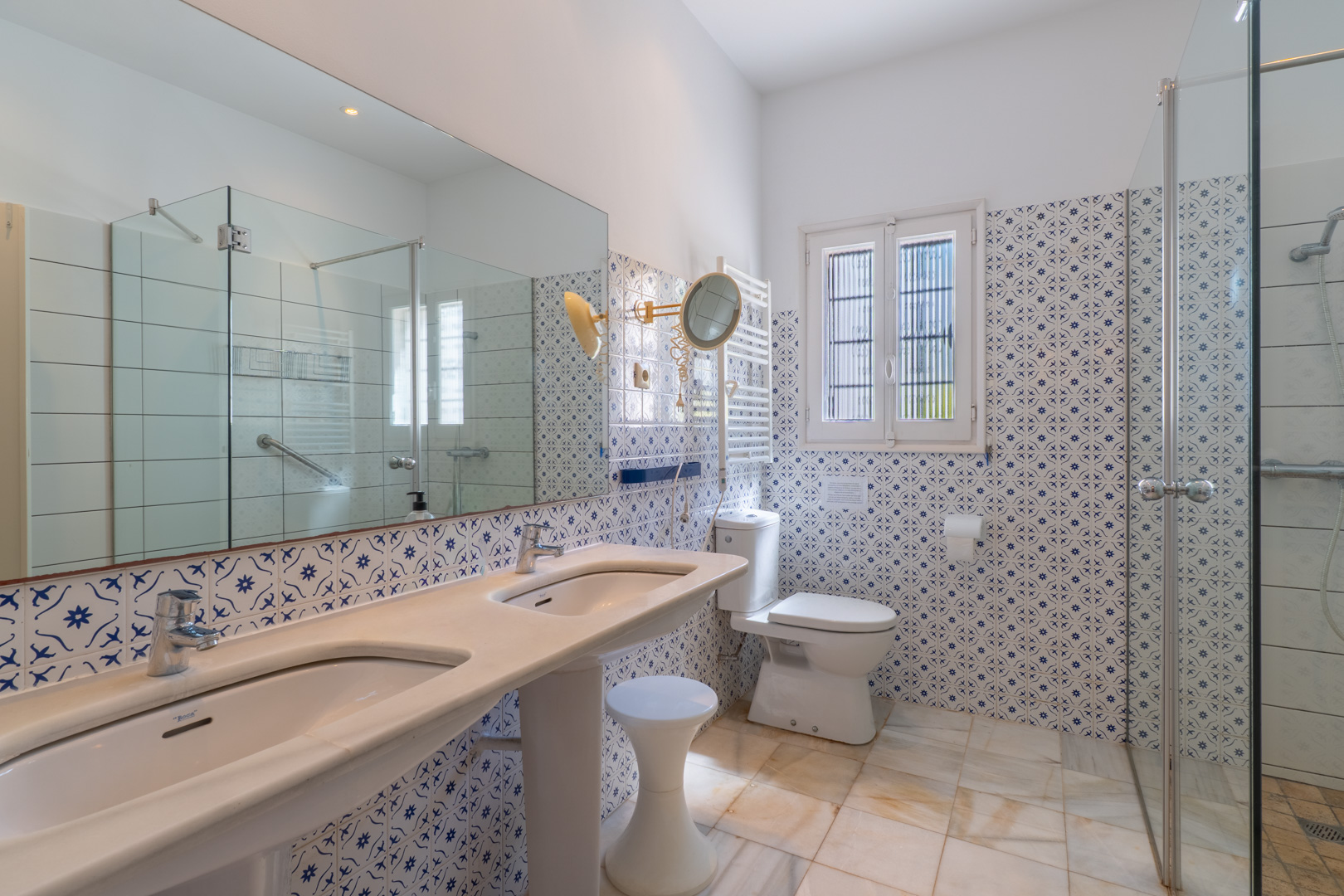 Cuarto de baño con lavabo doble de pedestal, azulejos decorativos y ducha con mampara de cristal.
