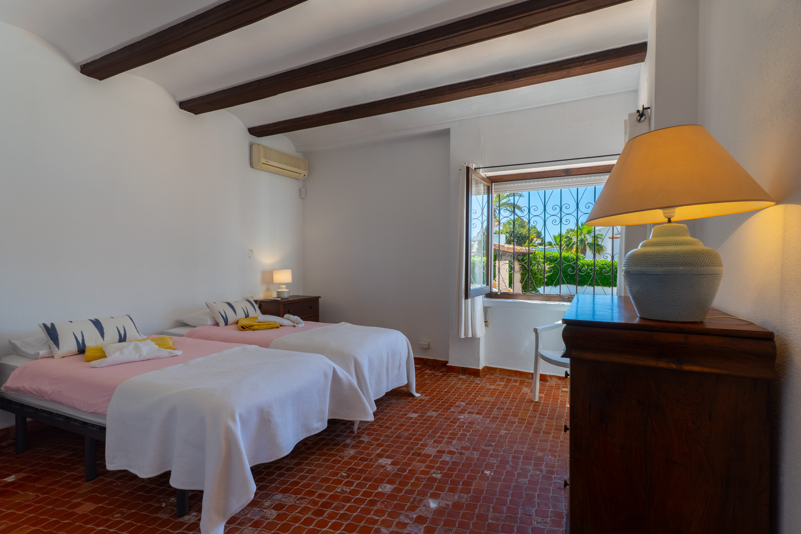 Dormitorio con dos camas, vigas de madera y suelo de terracota. Vistas al exterior.