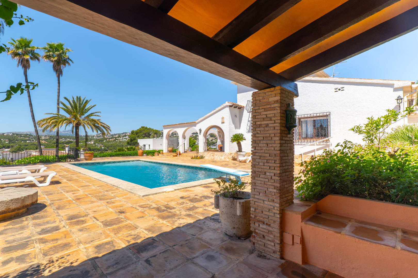 Vista de la piscina desde la terraza cubierta con vigas de madera y pilares de ladrillo.