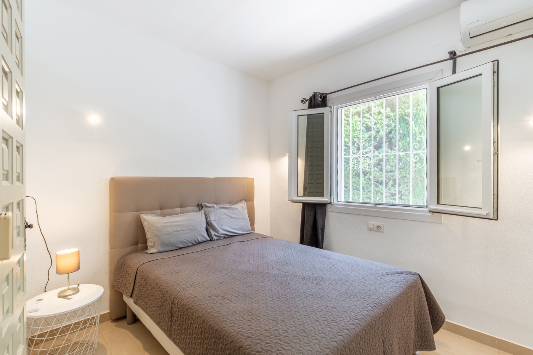 Dormitorio luminoso con cama de cabecero tapizado, gran ventana con rejas de seguridad y vistas a la vegetación, además de aire acondicionado. Dormitorio luminoso con cama de cabecero tapizado, gran ventana con rejas de seguridad y vistas a la vegetación, además de aire acondicionado.