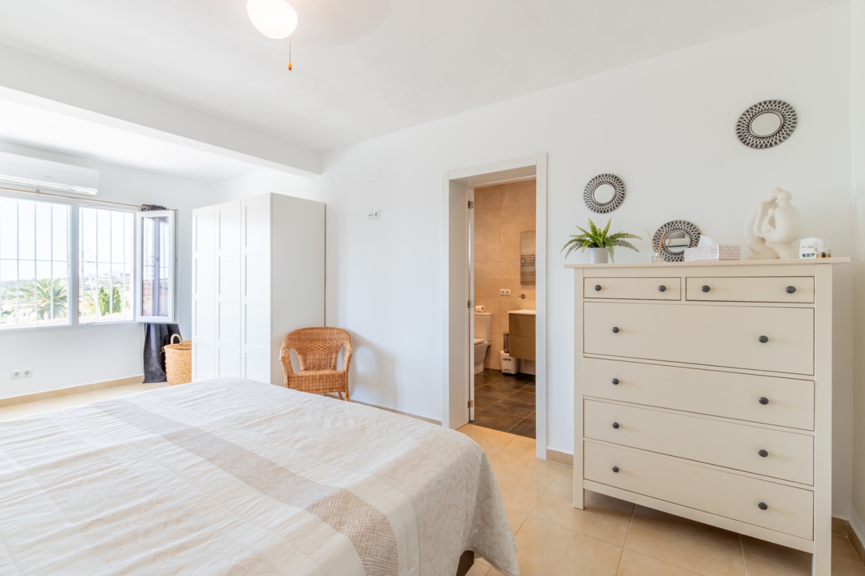 Dormitorio principal luminoso con cama doble, armario blanco y acceso directo a un baño privado. La ventana ofrece vistas a la vegetación exterior. Dormitorio principal luminoso con cama doble, armario blanco y acceso directo a un baño privado. La ventana ofrece vistas a la vegetación exterior.