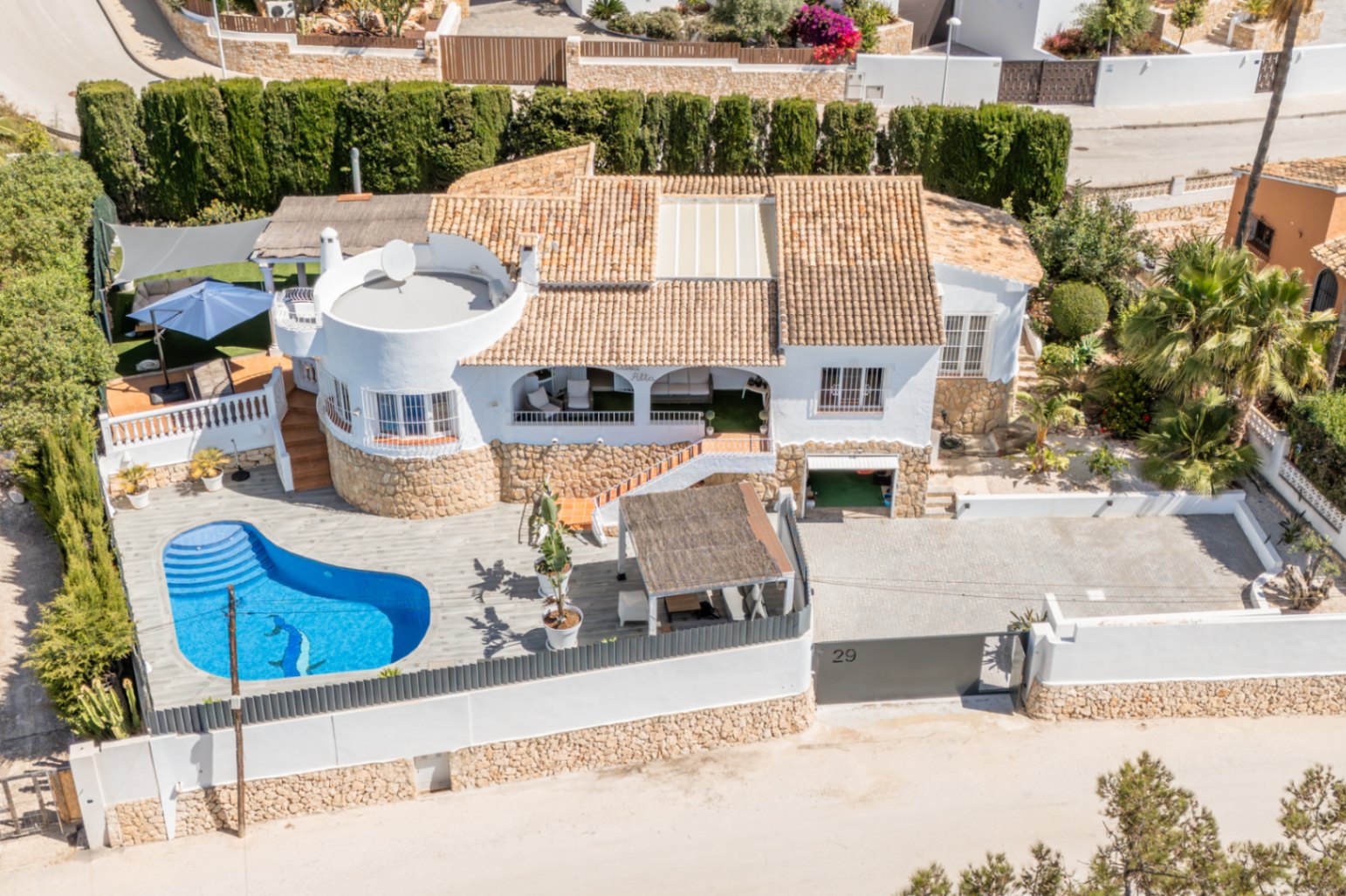 Vista aérea de la villa blanca con tejado de terracota y piscina privada en forma de riñón con mosaico de delfín. Destaca el amplio aparcamiento pavimentado y varias terrazas exteriores. Vista aérea de la villa blanca con tejado de terracota y piscina privada en forma de riñón con mosaico de delfín. Destaca el amplio aparcamiento pavimentado y varias terrazas exteriores.