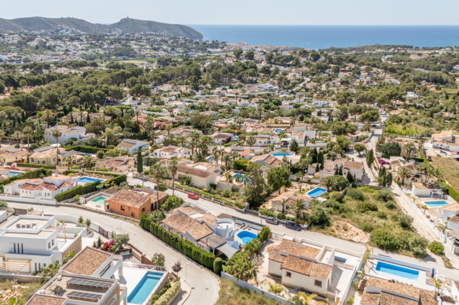 Vista aérea del área residencial de Moraira, destacando la densidad de villas con tejados de teja, piscinas privadas y el azul del Mediterráneo en el horizonte. Vista aérea del área residencial de Moraira, destacando la densidad de villas con tejados de teja, piscinas privadas y el azul del Mediterráneo en el horizonte.