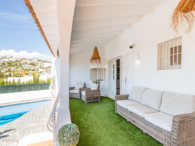 Amplia terraza cubierta con cómodos muebles de mimbre sobre césped artificial, ofreciendo vistas a la piscina privada y a las colinas residenciales bajo un cielo despejado.