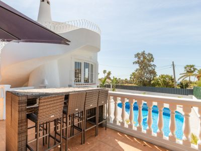 Amplia terraza exterior con barra de ratán y taburetes, con vistas a la piscina privada. Se aprecia la singular arquitectura espiral de la villa blanca bajo un cielo despejado.