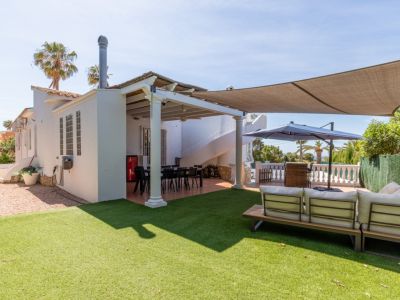 Amplio jardín con césped artificial y área de estar exterior. Terraza cubierta con mesa de comedor y escaleras de caracol, protegida por una vela de sombra.