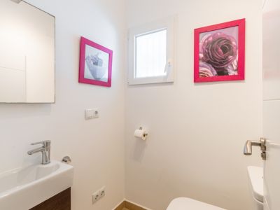 Aseo de cortesía con lavabo rectangular y grifería cromada. Destacan los detalles decorativos con marcos fucsia y una ventana que aporta luz natural.