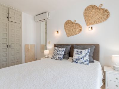 Dormitorio con cama confortable, cabecero gris, colcha blanca acolchada y cojines estampados. Armario empotrado panelado, aire acondicionado y decoraciones de corazones trenzados en la pared.