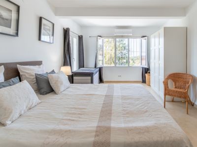 Dormitorio principal con cama doble, suelo de baldosas claras, armario blanco y ventana con rejas, ofreciendo vistas al exterior y aire acondicionado.