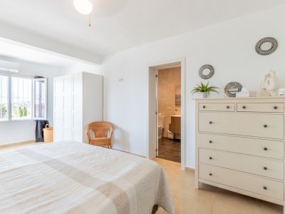 Dormitorio principal luminoso con cama doble, armario blanco y acceso directo a un baño privado. La ventana ofrece vistas a la vegetación exterior.