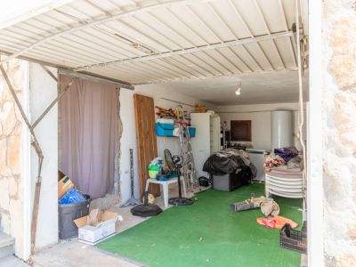 Espacio de garaje o almacén con techo de chapa y suelo de césped artificial. Contiene calentador de agua, nevera, escalera y diversos objetos de almacenamiento.