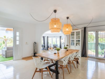 Luminoso comedor con mesa de madera maciza, lámparas colgantes de ratán y suelo de baldosas claras. Ofrece acceso directo a una terraza exterior y se conecta a la sala de estar a través de un arco.