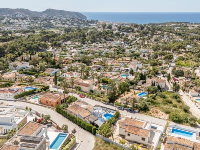 Vista aérea del área residencial de Moraira, destacando la densidad de villas con tejados de teja, piscinas privadas y el azul del Mediterráneo en el horizonte.