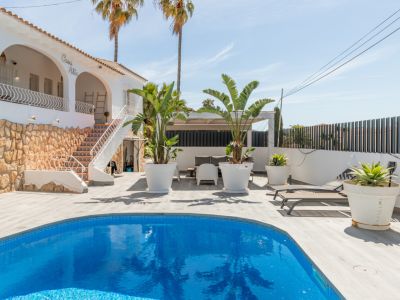 Vista exterior de la villa 'Casa Alta' con piscina de mosaico azul. La terraza de lamas claras rodea la piscina, junto a una escalera exterior con azulejos decorativos y base de piedra.