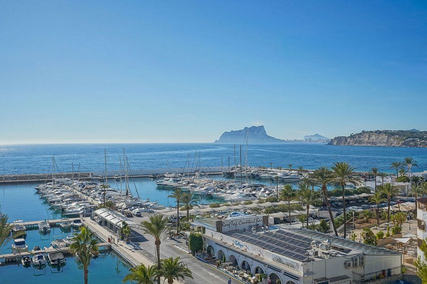 Vista panorámica del animado puerto deportivo de Moraira, repleto de yates y embarcaciones, con el mar azul y el icónico Peñón de Ifach al fondo. Vista panorámica del animado puerto deportivo de Moraira, repleto de yates y embarcaciones, con el mar azul y el icónico Peñón de Ifach al fondo.