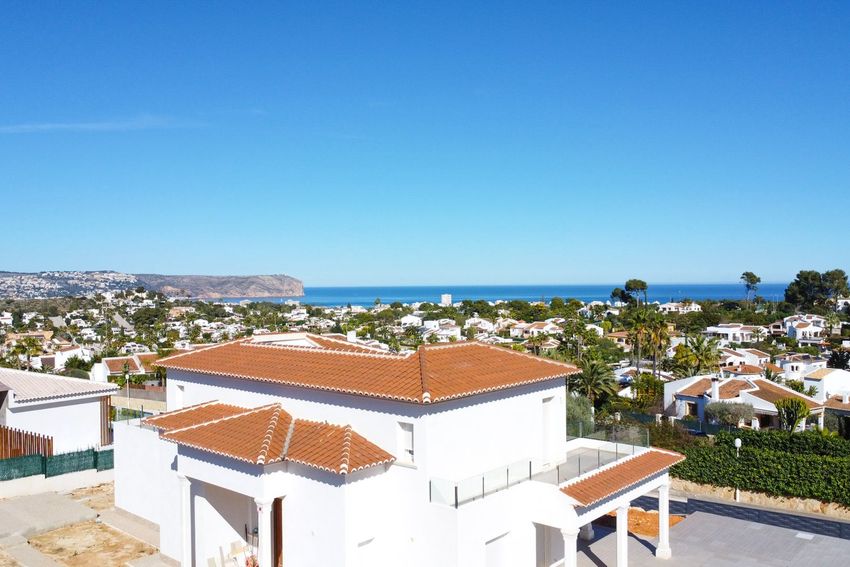 Vista aérea de una villa blanca con tejados de terracota y terraza con barandilla de cristal, ofreciendo vistas panorámicas al mar y la costa de Jávea. Vista aérea de una villa blanca con tejados de terracota y terraza con barandilla de cristal, ofreciendo vistas panorámicas al mar y la costa de Jávea.