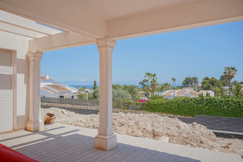 Vista desde una terraza con pérgola y pilares, ofreciendo panorámicas al mar sobre un futuro jardín y tejados mediterráneos. Vista desde una terraza con pérgola y pilares, ofreciendo panorámicas al mar sobre un futuro jardín y tejados mediterráneos.