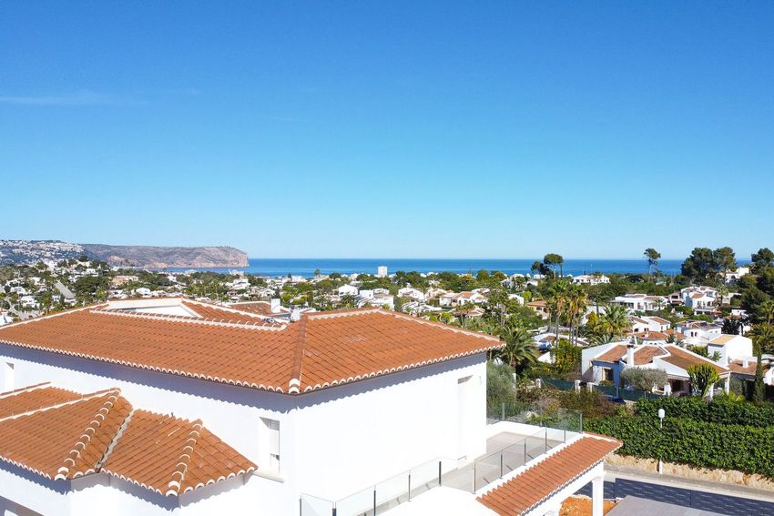 Vista elevada de la villa con tejado de teja tradicional y terraza moderna con barandilla de cristal, ofreciendo vistas al mar sobre la costa de Jávea. Vista elevada de la villa con tejado de teja tradicional y terraza moderna con barandilla de cristal, ofreciendo vistas al mar sobre la costa de Jávea.