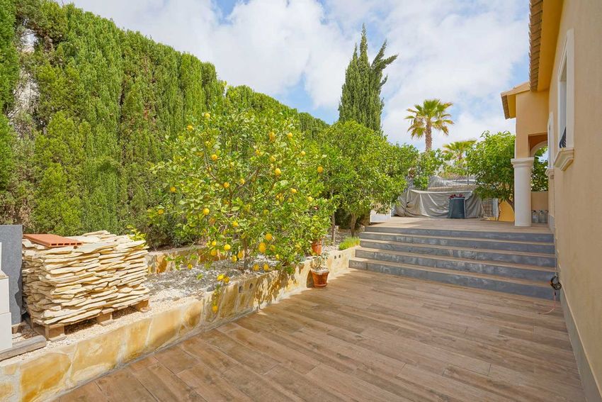Terraza exterior con suelo de imitación madera, bordeada por un muro de piedra y limoneros cargados de fruta, con materiales de construcción apilados.
