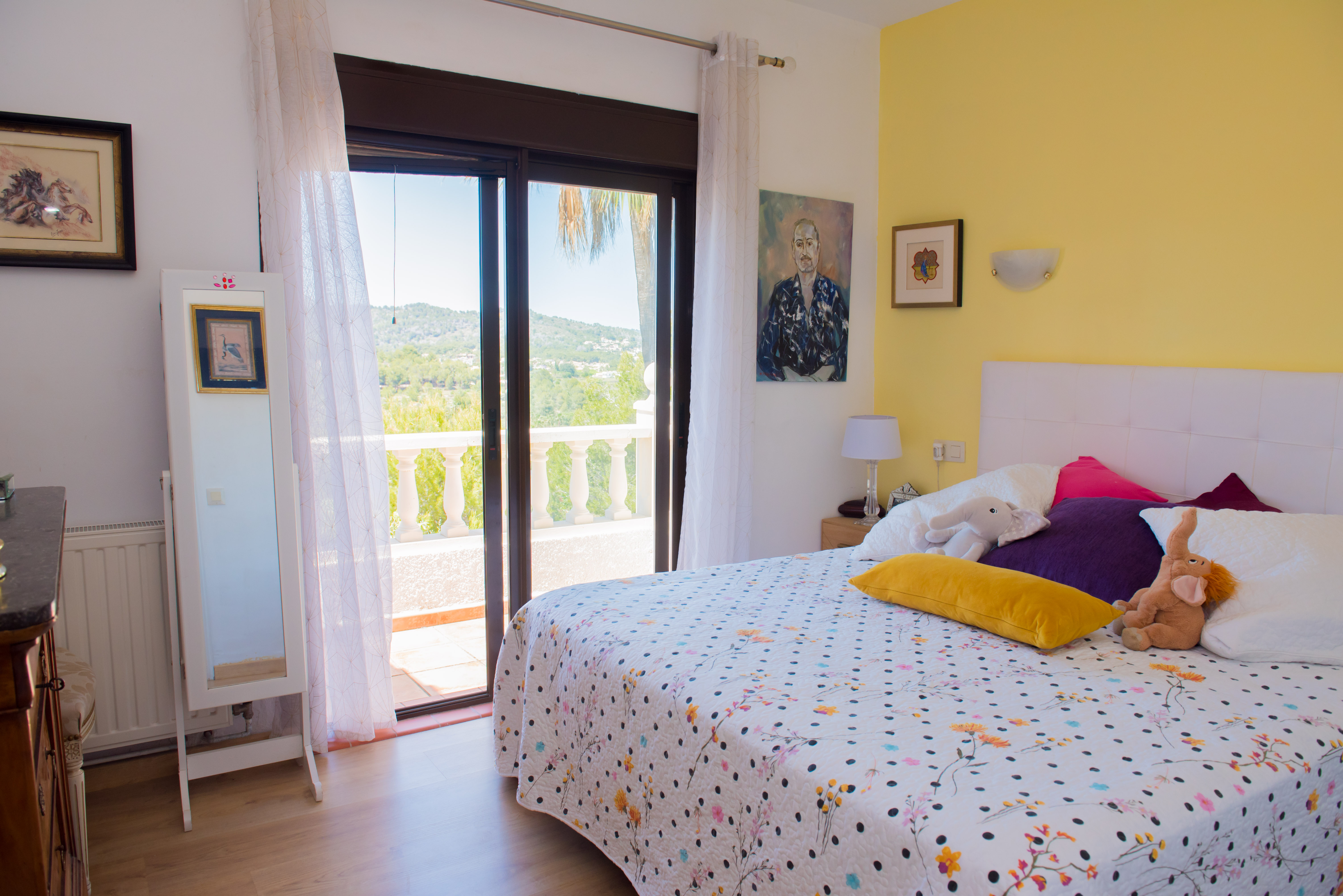 Dormitorio luminoso con acceso a balcón. Pared amarilla y ropa de cama estampada.