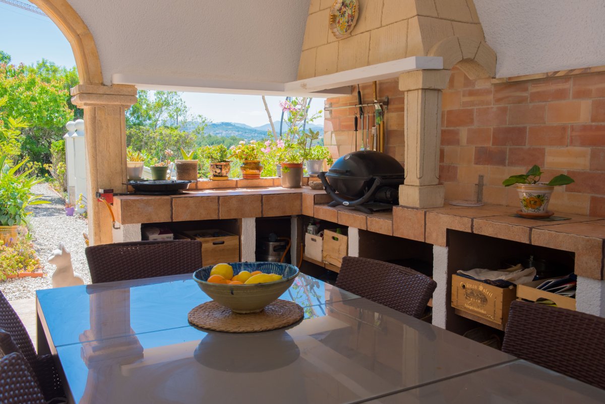 Naya cubierta con cocina de verano de obra, barbacoa de ladrillo y mesa de comedor. Vistas al jardín y colinas desde este espacio exterior.