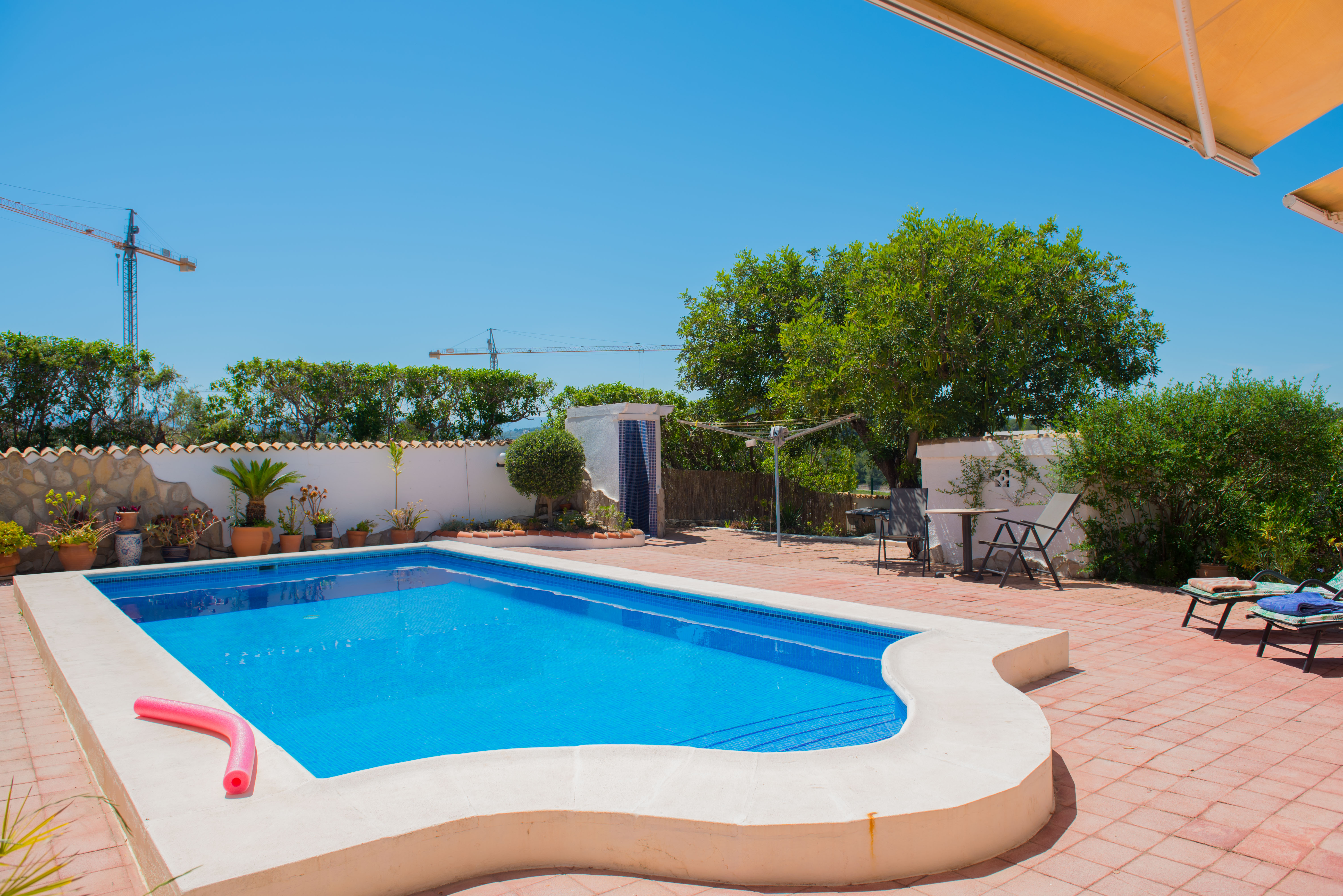 Piscina con mosaicos azules y borde de cemento blanco en patio de baldosas rojas.