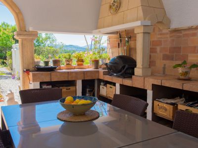 Naya cubierta con cocina de verano de obra, barbacoa de ladrillo y mesa de comedor. Vistas al jardín y colinas desde este espacio exterior.