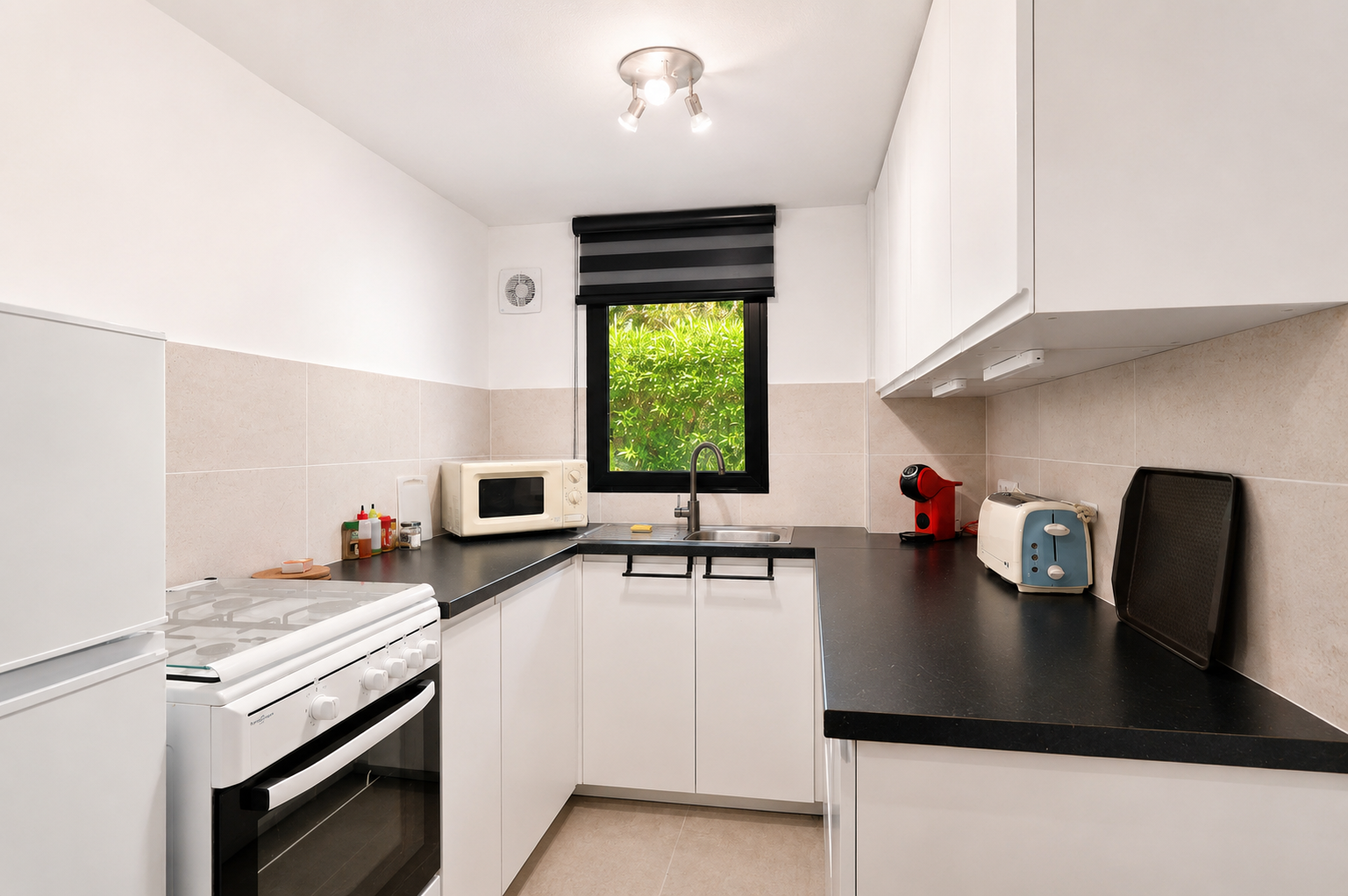 Cocina luminosa con encimeras negras, armarios blancos y ventana con vistas al jardín.