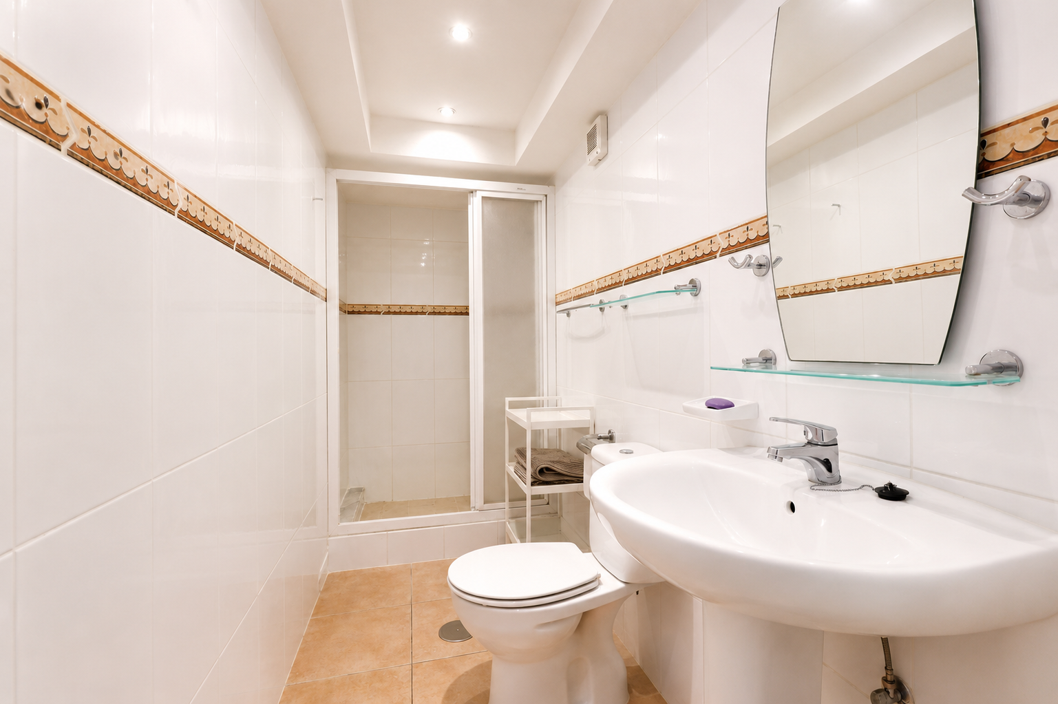 Cuarto de baño con azulejos blancos, cenefa decorativa y suelo cerámico color tierra.
