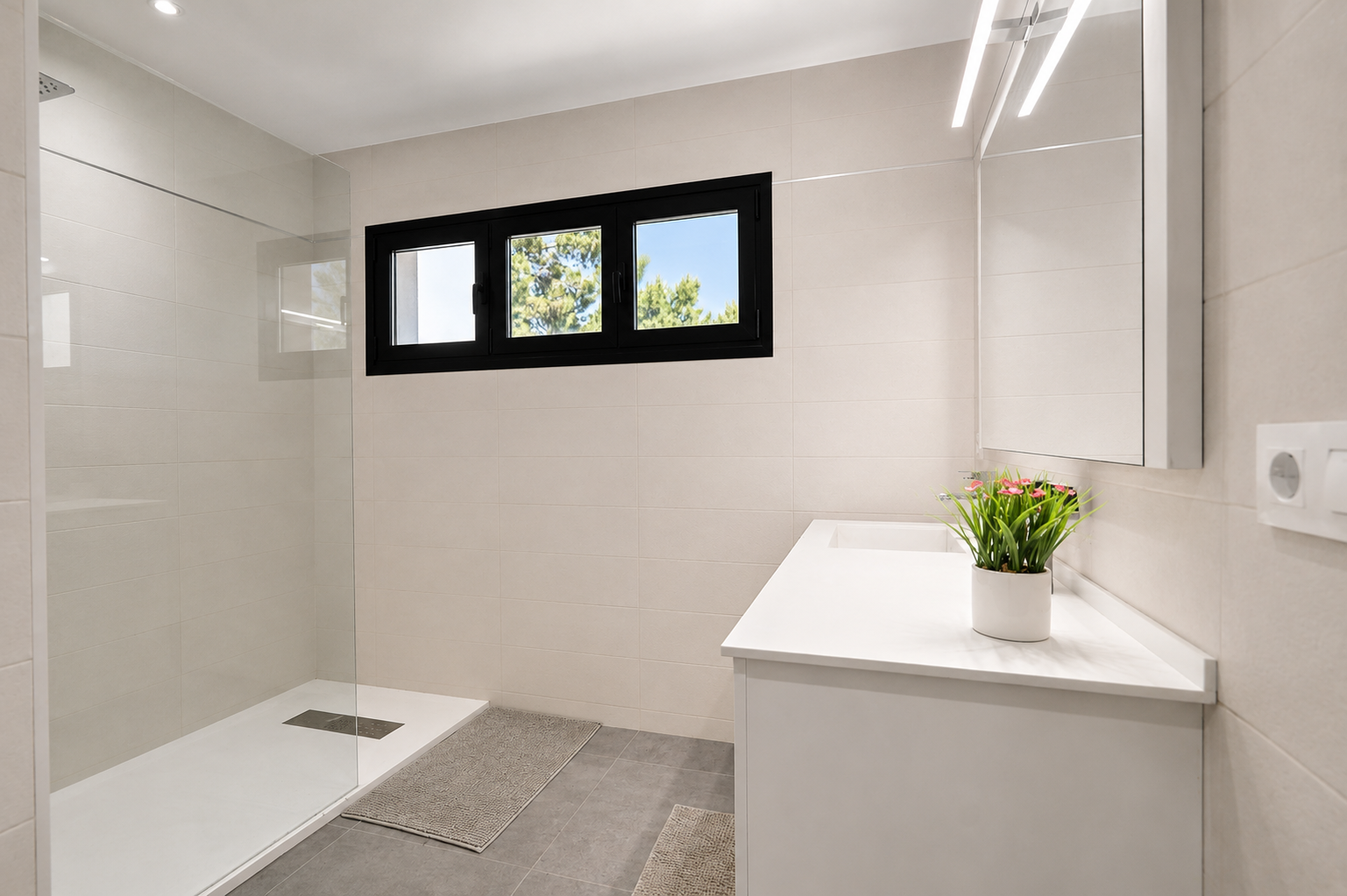 Cuarto de baño moderno con ducha de vidrio, lavabo blanco y ventana con marco negro que ilumina el espacio.