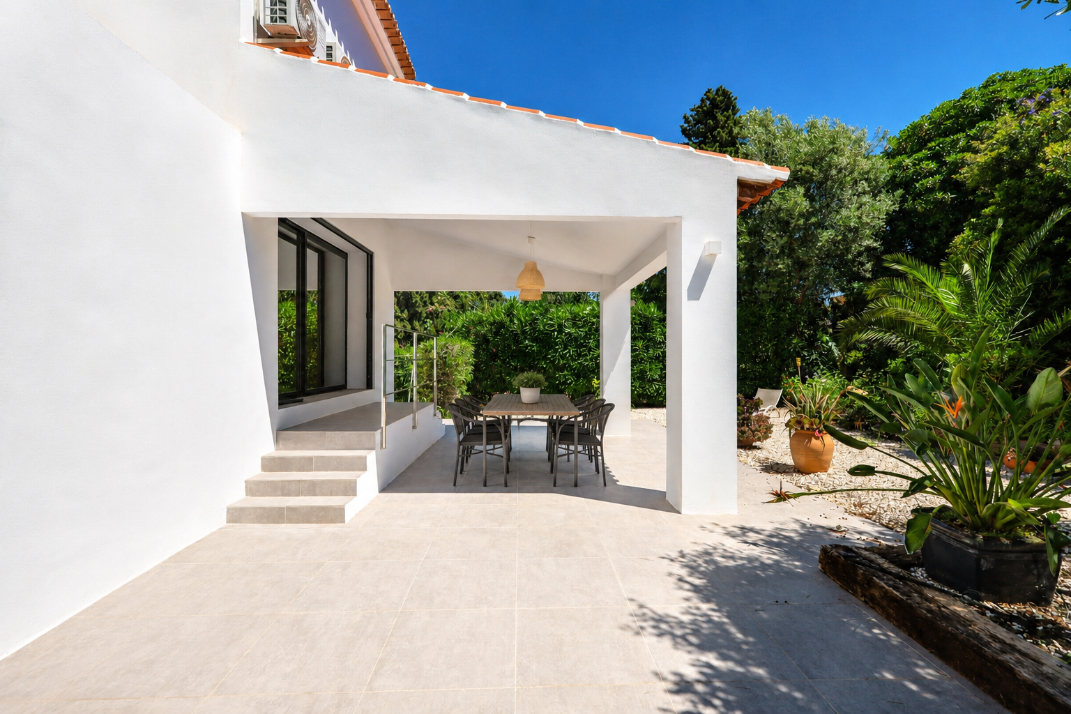 Naya cubierta con mesa de comedor, rodeada de jardines exuberantes y acceso a la villa.