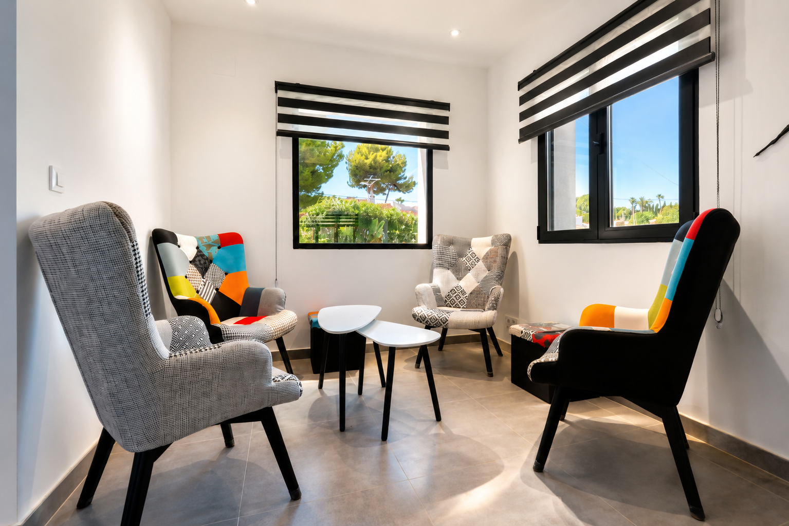 Sala de estar luminosa con sillas de diseño y vistas al jardín a través de ventanas con persianas.