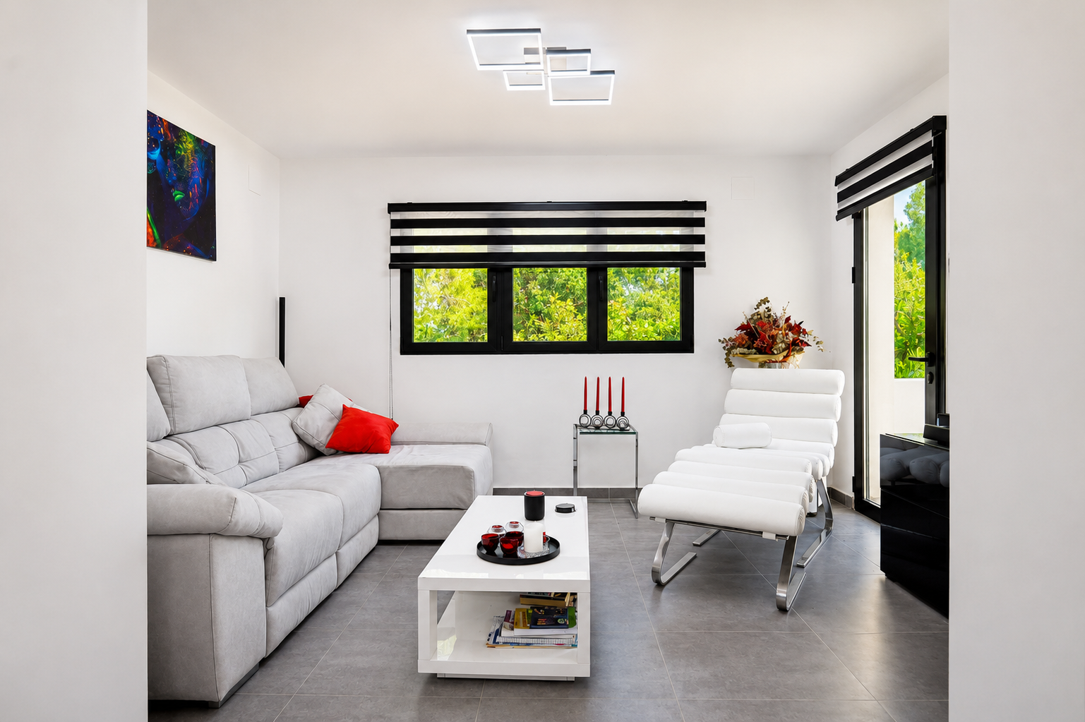Salón luminoso con sofá gris, butaca moderna blanca y detalles decorativos en rojo.