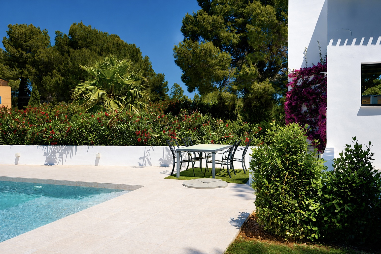 Vista de la piscina con borde de piedra clara y área de comedor exterior rodeada de vegetación.