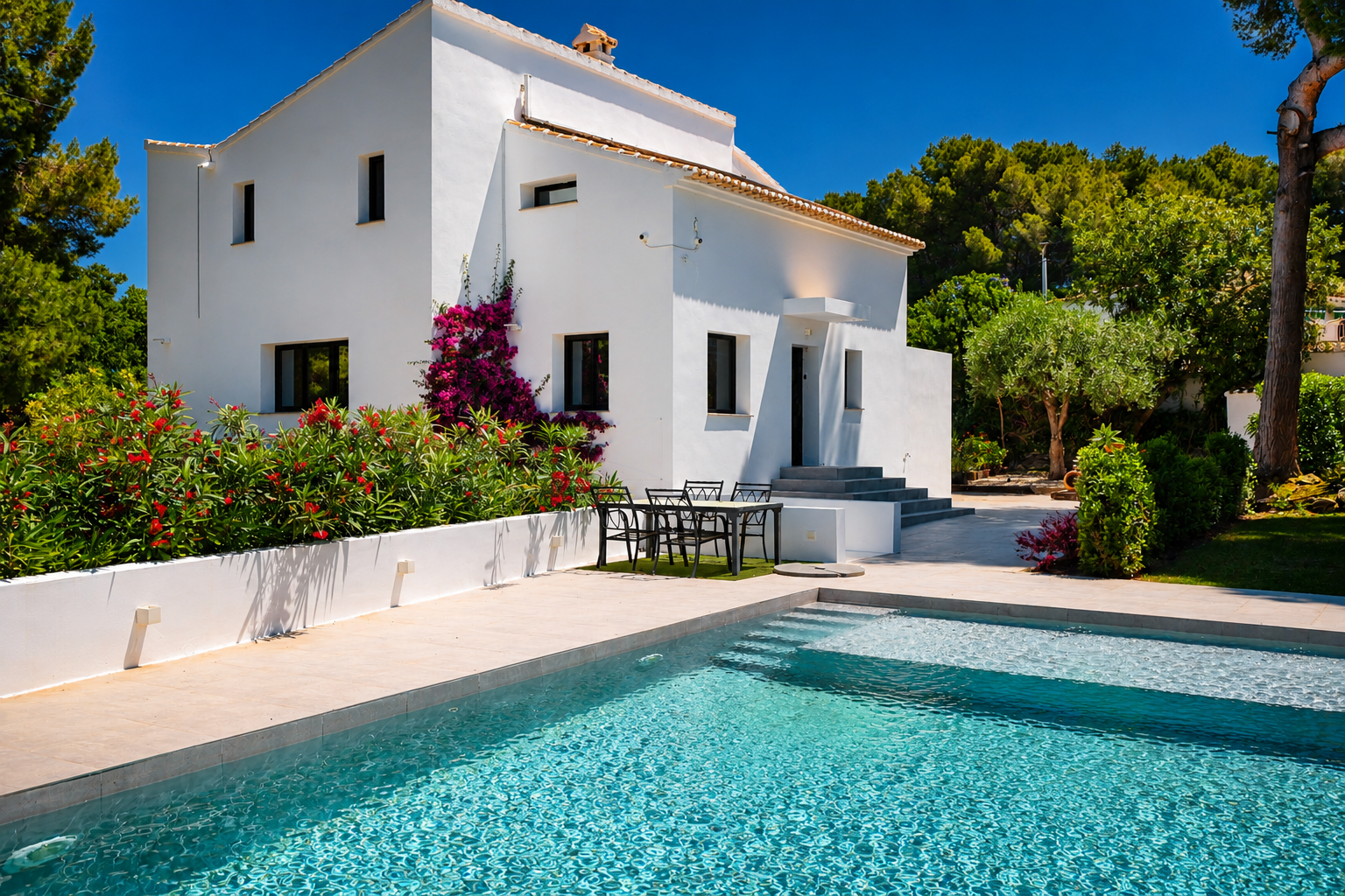 Vista de la piscina turquesa con acceso escalonado y la fachada blanca de la villa con buganvillas.