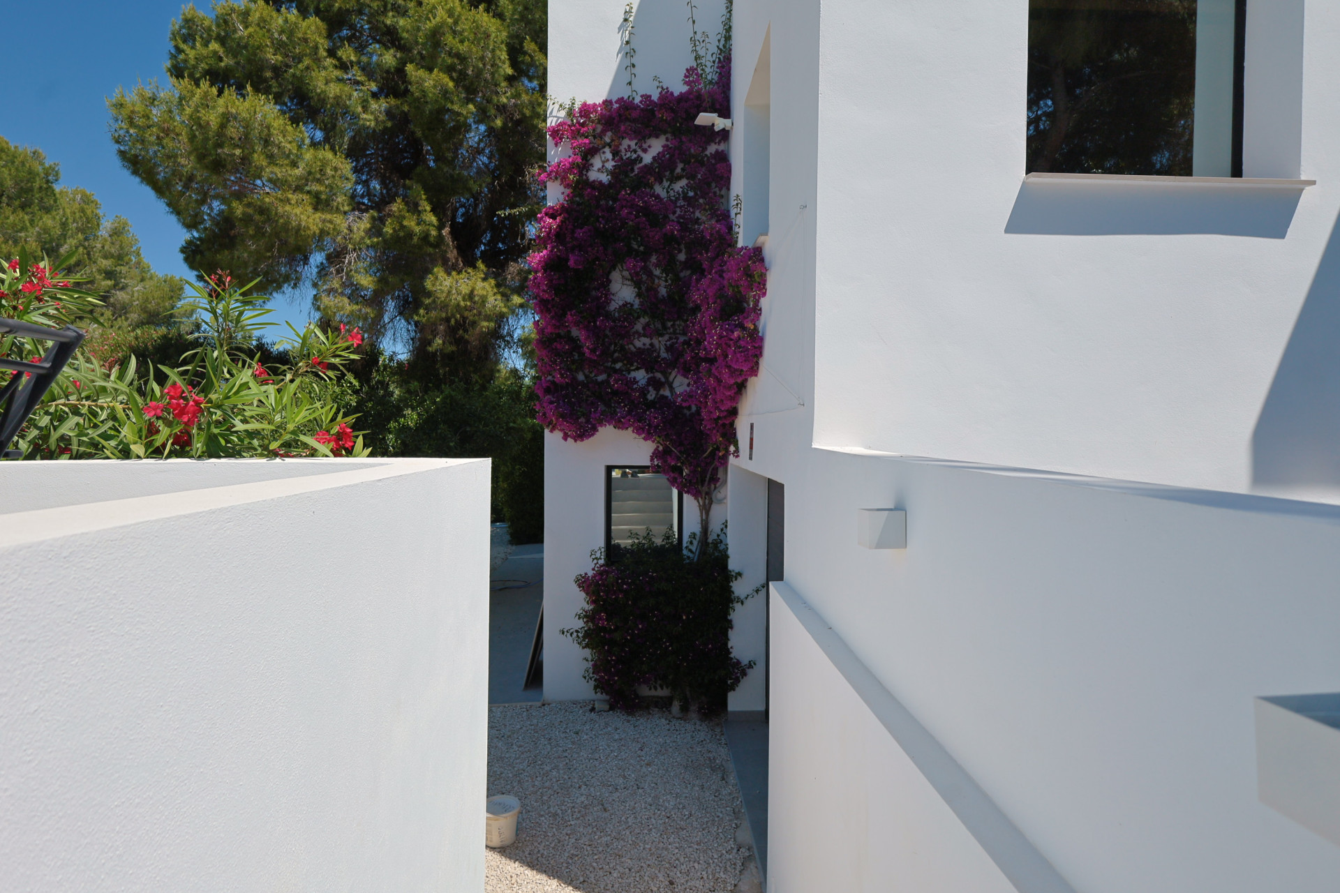 Vista exterior de la villa, con buganvillas floreciendo en la fachada blanca y grava clara en el suelo.