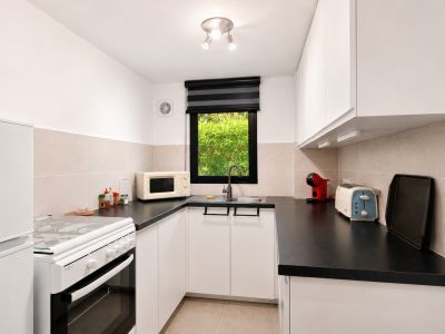 Cocina luminosa con encimeras negras, armarios blancos y ventana con vistas al jardín.