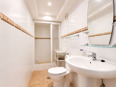 Cuarto de baño con azulejos blancos, cenefa decorativa y suelo cerámico color tierra.