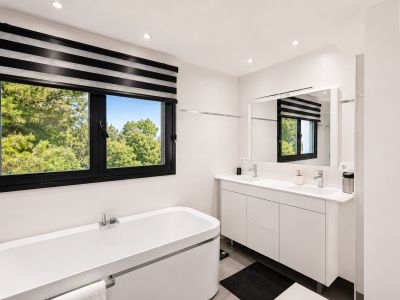 Luminoso baño con ventana de marco negro y vistas al exterior, bañera blanca y tocador doble con espejo.