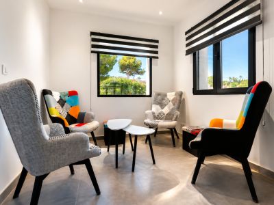 Sala de estar luminosa con sillas de diseño y vistas al jardín a través de ventanas con persianas.