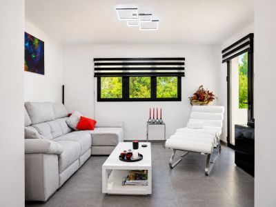 Salón luminoso con sofá gris, butaca moderna blanca y detalles decorativos en rojo.
